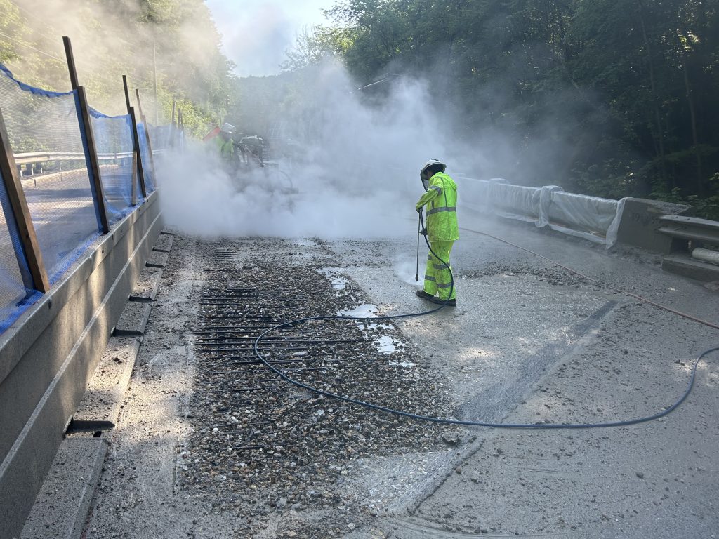 A man performing hydrodemolition with a handlance on a bridge deck.