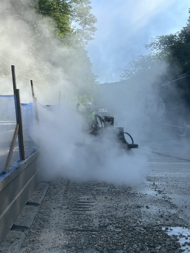 A man performing hydrodemolition with a robot on a bridge deck.