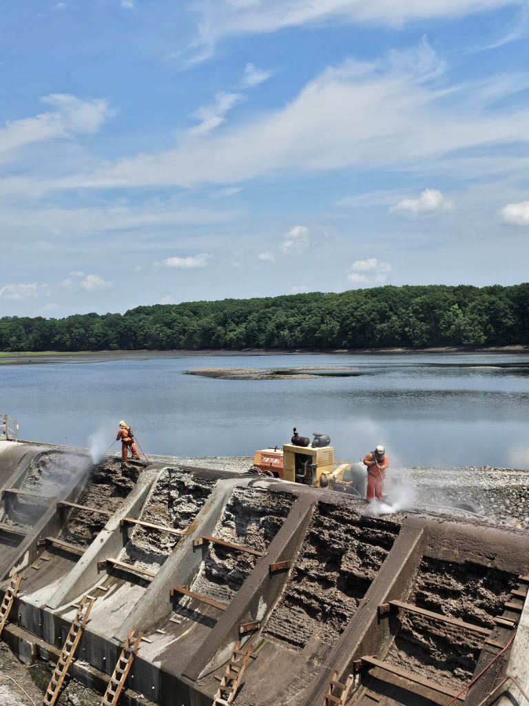 Operators using hand lances on the dam face for targeted removal of concrete.