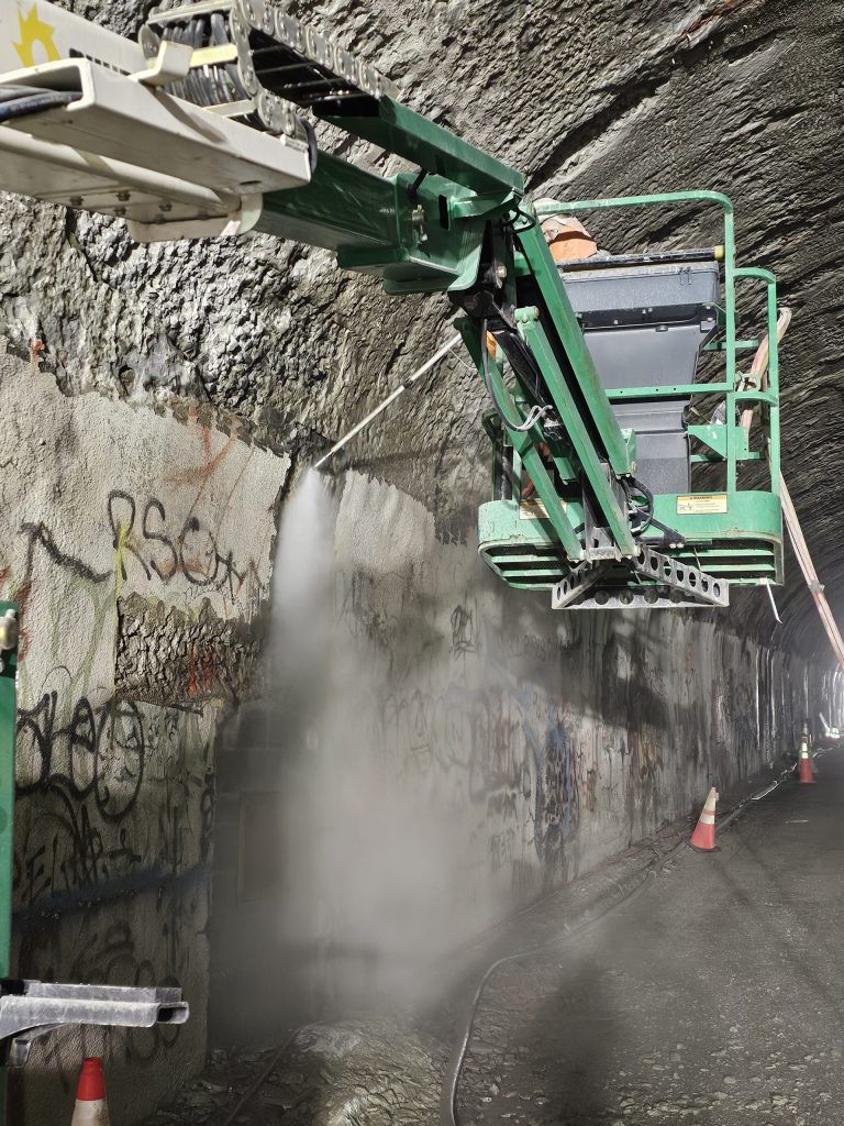 An operator using a hand lance to perform hydrodemolition of the gunnite on the tunnel side walls.